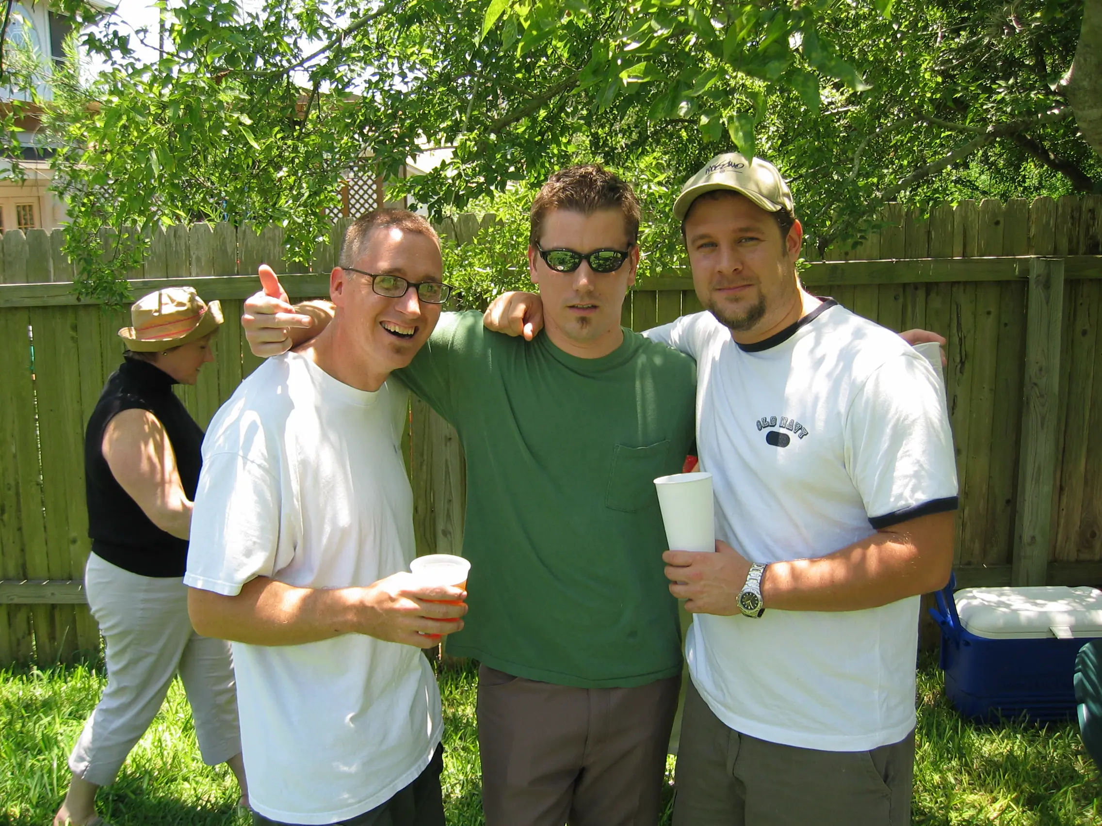 Three friends with their arms around each other holding cups at a backyard party