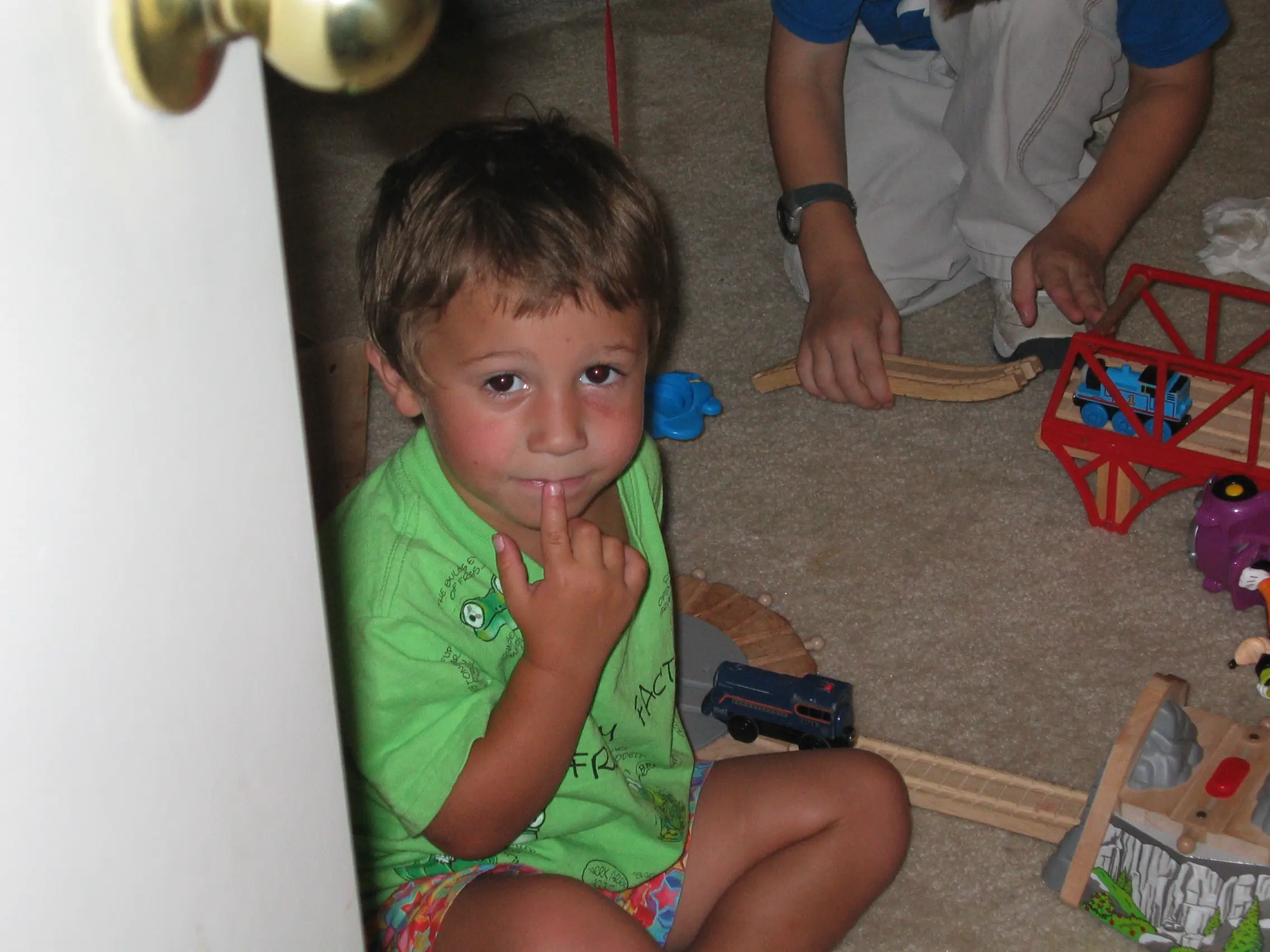 A young boy in a green shirt sitting on the floor with a wooden train set