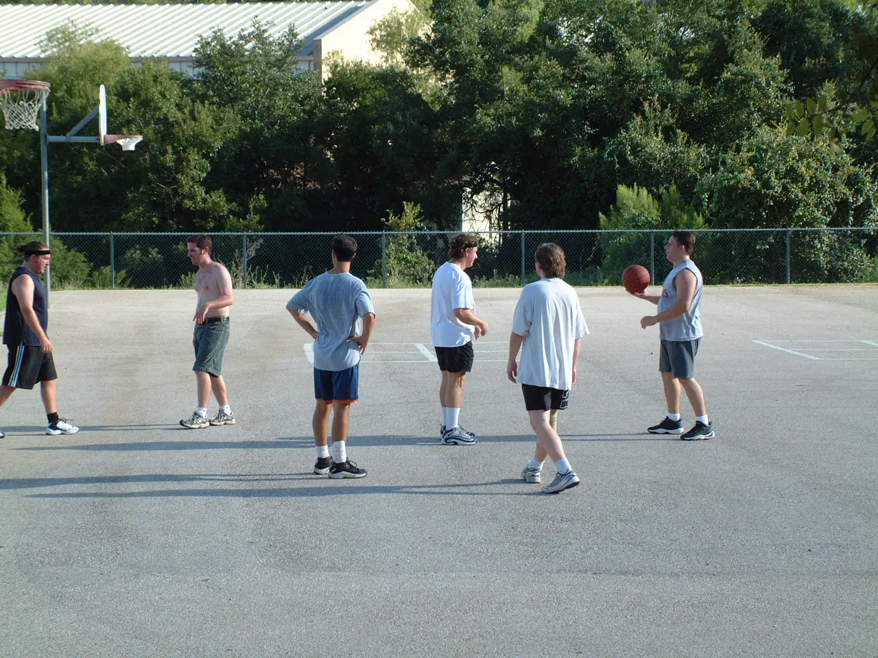 Six coworkers standing around an outdoor basketball court after work, one holding the ball
