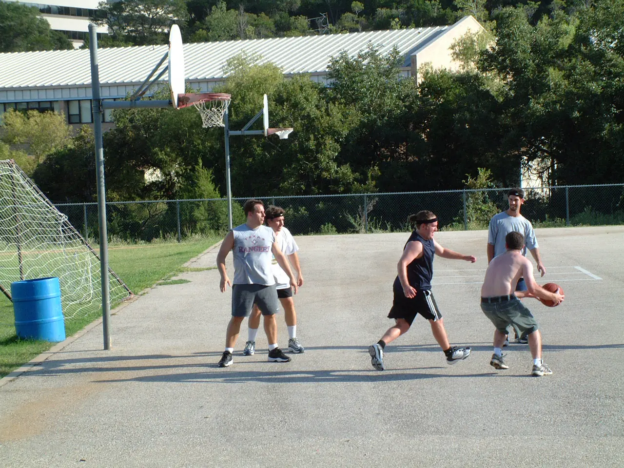A shirtless player driving to the basket during a pickup game while others defend