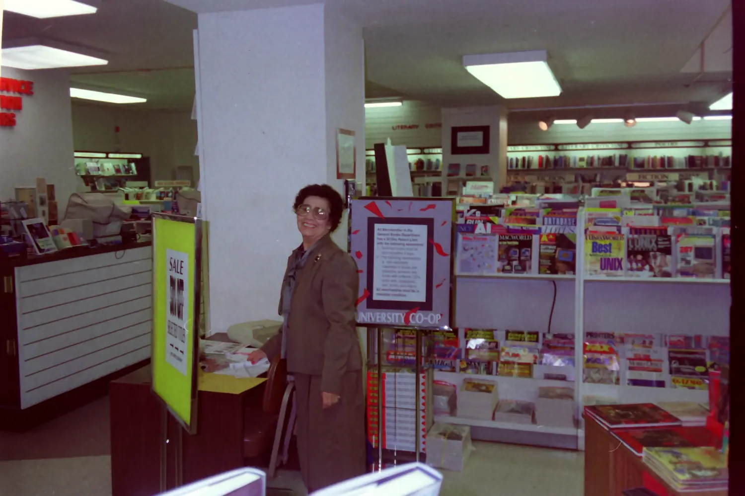 A coworker in the General Books section of the University Co-op in 1993, next to a sale sign and the magazine racks